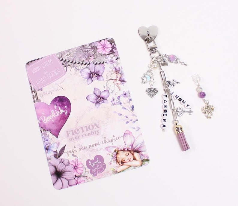 Decorative kindle accessories arranged beside a kindle paperwhite inside a clear kindle case featuring watercolor kindle insert, charm keychain attachment, and dust plug charm. Designed for readers who enjoy decorating their kindle case, kindle sleeve, or ereader case with kindle stickers, kindle skins, kindle decorations, and aesthetic kindle accessories inspired by cozy reading nights.