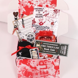 Blind Date with a Kindle mystery box for book lovers featuring a kindle insert for clear case, kindle charms, kindle dust plug charm, charm keychain, cozy socks, bookish stickers, sweet treat, and hot cocoa arranged as a cozy kindle accessories gift set. Perfect for decorating a kindle paperwhite or ereader case with cute kindle decorations, kindle stickers, and aesthetic kindle accessories that transform your reading night into a relaxing booklover experience.