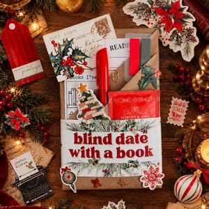 May include: A brown paper-wrapped book labeled Blind Date with a Book, featuring a red pen, a Harney & Sons tea packet, a bookmark, and a paper clip. The package is decorated with stickers of a book stack, holly, and a snowflake.
