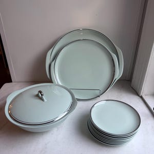 Könnte beinhalten: Ein Set aus hellblauen und silbernen Servierplatten. Das Set enthält eine große Platte, eine kleinere Platte, eine Schüssel mit Deckel und einen Stapel von sechs kleineren Tellern.