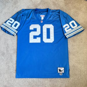 Pode incluir: Uma camisa de futebol azul com o número 20 na frente e nas costas. A camisa tem o logotipo dos Detroit Lions nas mangas e o logotipo da NFL no peito. A camisa é feita pela Starter e tem uma etiqueta que diz "1996".