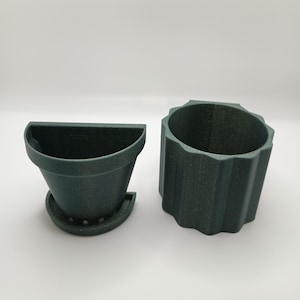 May include: Two dark green plastic plant pots. One is a round pot with a textured surface. The other is a half-round pot with drainage holes.