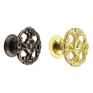 May include: Two ornate cabinet knobs, one in antique brass and one in polished brass, with a decorative, intricate, circular design.