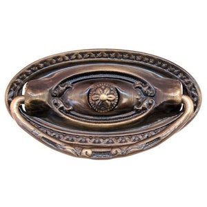 May include: An oval-shaped, antique brass cabinet pull with a decorative floral design and a ring handle.