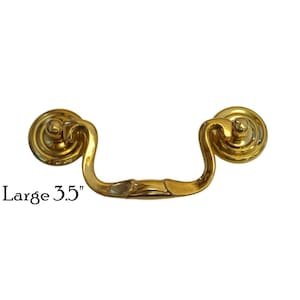 May include: A gold-toned metal cabinet pull with a decorative design. The pull is 3.5 inches long and has a rounded shape. It is labeled "Large 3.5" in the image.