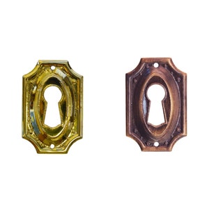 May include: Two keyhole escutcheons, one gold and one bronze, with ornate detailing around the edges.