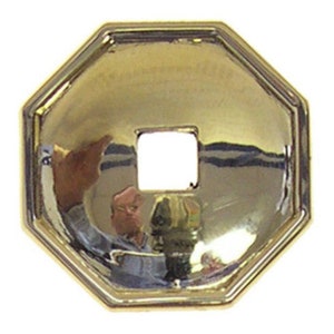 May include: A gold-colored octagonal metal plate with a square hole in the center. The plate has a slightly domed shape and a smooth, polished surface.