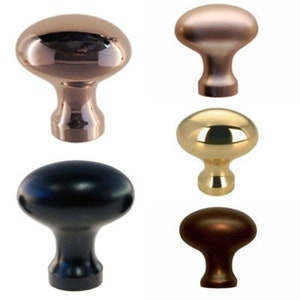 May include: Four cabinet knobs in different finishes: polished brass, black, copper, and polished nickel. Each knob has a rounded oval shape with a raised center.