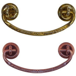 May include: Two cabinet pulls, one in gold and one in copper. Both have a decorative, ornate design and a ring-shaped handle.