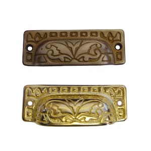 May include: Two ornate gold drawer pulls with a decorative floral design. The top pull is a darker gold color, while the bottom pull is a brighter gold color.