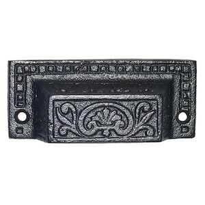 May include: Black cast iron drawer pull with an ornate floral design. The pull has a rectangular shape with rounded corners and a beveled edge.