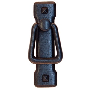 May include: Black metal door pull with a rectangular shape and a ring handle. The pull has a hammered finish and two square accents at the top and bottom.