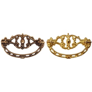 May include: Two ornate metal drawer pulls, one in a brass finish and one in a gold finish. Both pulls have a decorative, scroll-like design.
