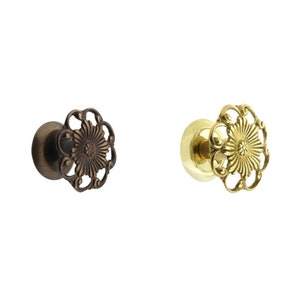 May include: Two decorative door knobs with a floral design. The knob on the left is a dark bronze color and the knob on the right is a polished brass color.