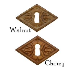 May include: Two wooden keyhole covers, one in walnut and one in cherry, with a diamond shape and intricate carvings around the keyhole.