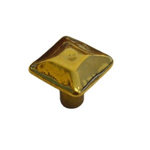 May include: A square-shaped, gold-toned cabinet knob with a raised, slightly rounded top.