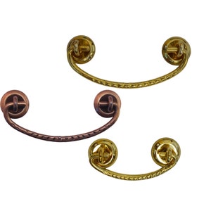 May include: Three decorative cabinet pulls, two gold and one copper. The pulls are shaped like a half-circle with a decorative design on the front.