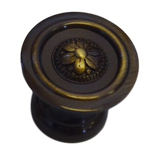 May include: A round, dark brown cabinet knob with a raised, ornate, gold-colored flower design.