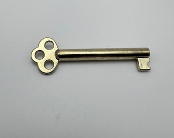 Op de afbeelding: Een zilverkleurige sleutel met een viergaats klaverbladvormig kop en een gekartelde rand.