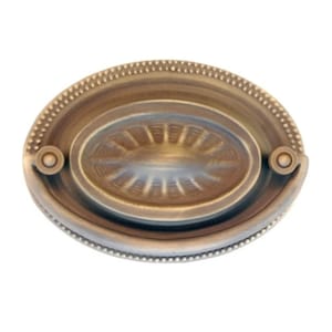 May include: An antique-style brass drawer pull with an oval shape. The pull features a central oval design with a textured pattern and is surrounded by a beaded border. Two circular mounting points are on either side of the pull.
