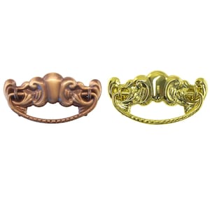 May include: Two ornate drawer pulls. One is bronze-colored, the other is gold-colored. Both have a curved handle and decorative scrollwork. These pulls are likely for furniture such as cabinets or drawers.