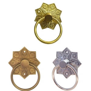 May include: Three decorative door pulls with a starburst design and a ring handle. The pulls are in gold, brass, and silver.