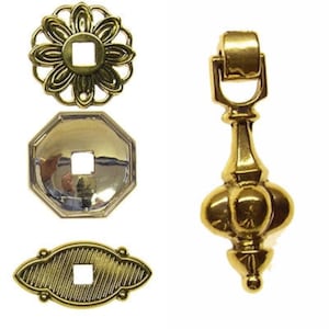 May include: Four gold-toned metal cabinet hardware pieces. The pieces include a flower-shaped knob, a round knob, an oval knob, and a decorative pull with a round knob at the bottom.