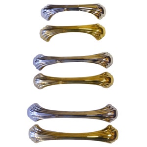 May include: Six decorative cabinet pulls in a mix of silver and gold finishes. Each pull has a curved, ribbed design with rounded ends. The pulls are arranged in pairs, alternating between silver and gold.