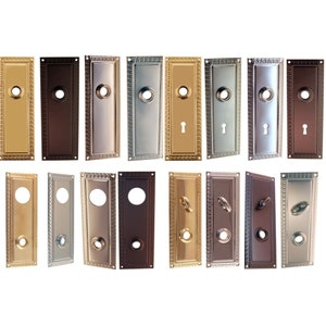 May include: A set of 12 decorative door plates in various finishes, including brass, nickel, and bronze. Each plate features a rectangular shape with a decorative border and a keyhole.