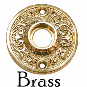 May include: A brass door knob escutcheon with an ornate design. The escutcheon is round and has a hole in the center for the knob. The escutcheon is decorated with a floral pattern.