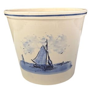 May include: Cream ceramic planter with a blue nautical design. The planter has a blue sailboat scene and a blue rim. The design includes a sailboat on the water, clouds, and birds.