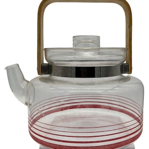 May include: A clear glass teapot with a wooden handle and red stripes around the bottom. The teapot has a silver metal band around the middle.