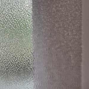 May include: A close-up of a textured glass window pane. The glass has a pattern of small, raised bumps that create a rippled effect. The light shines through the glass, creating a soft, diffused glow.