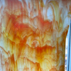 May include: A close-up of a piece of stained glass with a swirling pattern of orange, yellow, and white.