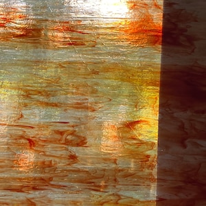 Op de afbeelding: Een close-up van een getextureerd glazen paneel met een verticale lijn in het midden. Het glas heeft een gelaagd, marmerachtig effect in tinten bruin, oranje en geel.