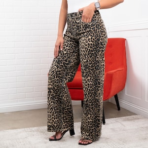May include: Wide-leg leopard print pants in shades of tan and black. The pants have a high waist and a relaxed fit. The model is wearing black sandals. The pants are made of a soft, flowing fabric.
