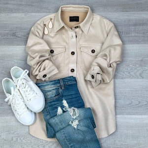 May include: A beige suede shirt with a button-down front and two flap pockets. The shirt is paired with blue denim jeans and white sneakers.