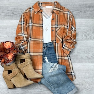 May include: A brown and white plaid flannel shirt with a white v-neck shirt underneath. The shirt is worn with blue jeans and brown suede ankle boots.