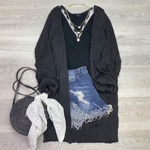 May include: A black crochet cardigan with a long, loose fit. The cardigan has a V-neck and long sleeves. It is paired with a black tank top, denim shorts, and a white bandana.