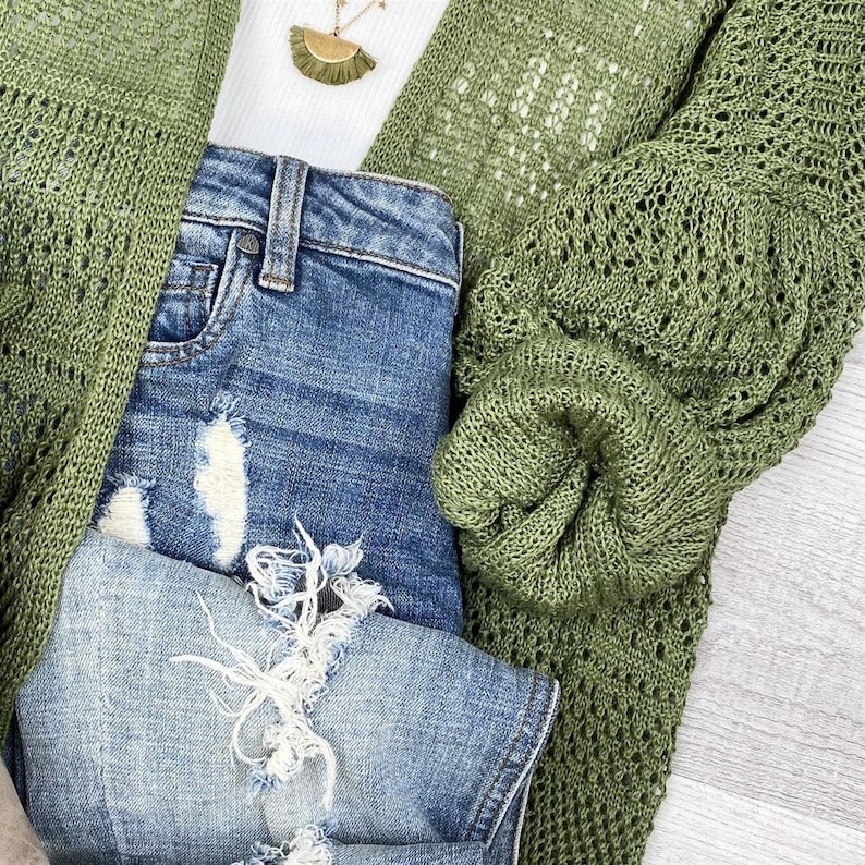 May include: A green crochet cardigan with a light blue denim shirt underneath. The cardigan has a loose fit and a delicate open weave.
