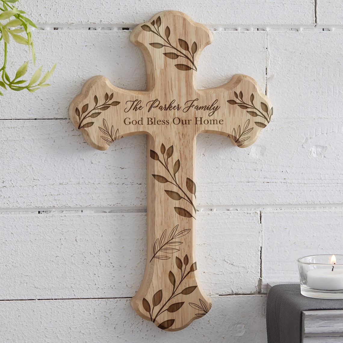 May include: A wooden cross with a light brown finish, featuring engraved leaf designs and the text "The Parker Family God Bless Our Home." The cross is mounted on a white, textured wall, suitable for home decor.
