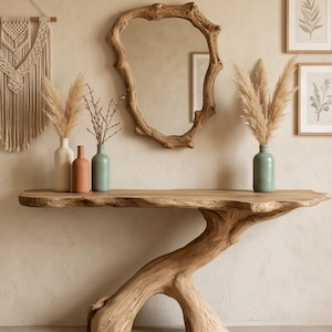 Puede incluir: Una consola de madera rústica con un diseño natural y orgánico. La mesa presenta una tapa de borde vivo y una pata en forma de rama. Jarrones en blanco, terracota y verde contienen plantas secas. Un espejo de madera y grabados botánicos enmarcados completan la decoración.