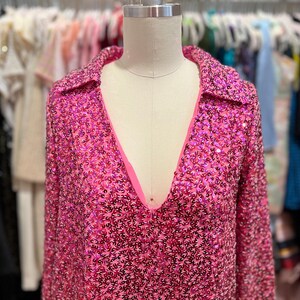 Puede incluir: Una camisa de manga larga de lentejuelas rosa con cuello y escote en V.