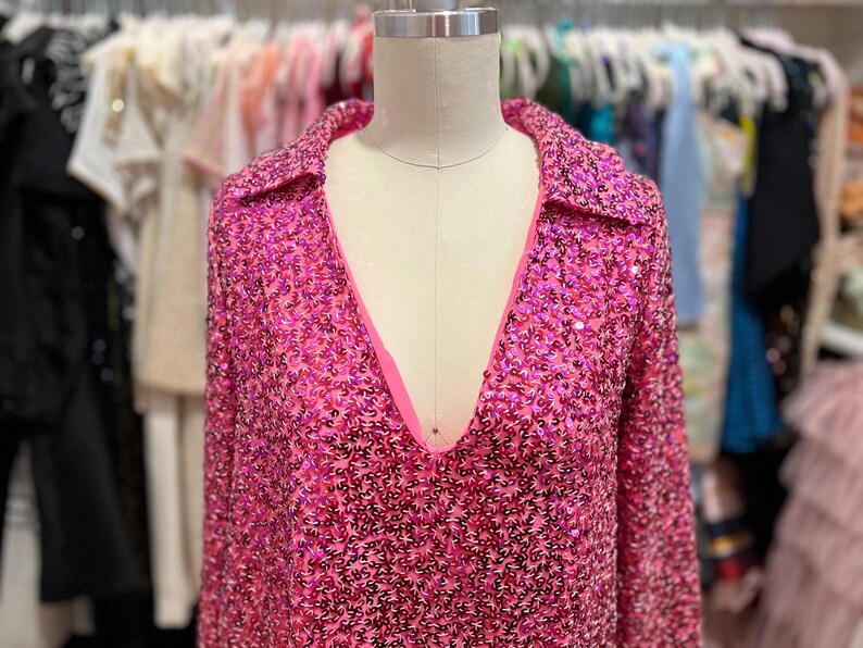 Puede incluir: Una camisa de manga larga de lentejuelas rosa con cuello y escote en V.