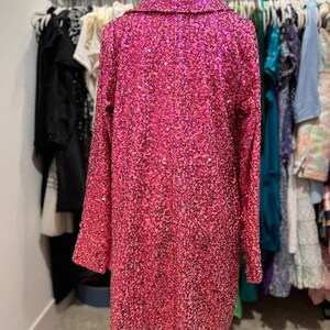 Puede incluir: Una chaqueta larga de manga larga de lentejuelas rosa con cuello.
