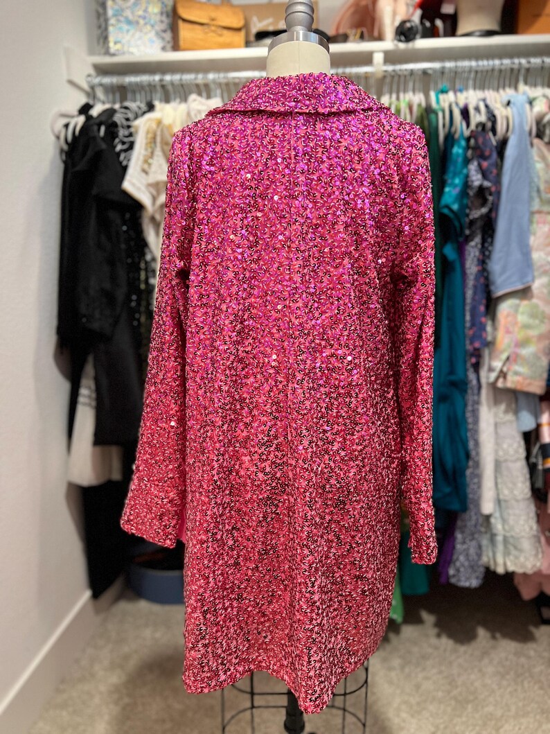 Puede incluir: Una chaqueta larga de manga larga de lentejuelas rosa con cuello.