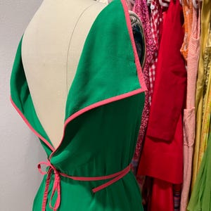 Puede incluir: Un vestido verde con ribete rosa y un lazo en la cintura. El vestido tiene la espalda baja y es sin mangas.