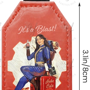 Op de afbeelding: Rode Fallout sleutelhanger, 8 cm lang, met een retro illustratie van een vrouw in een blauwe overall met de tekst "It's a Blast!" en "Fallout". Inclusief een metalen sleutelhanger en een zwarte band.