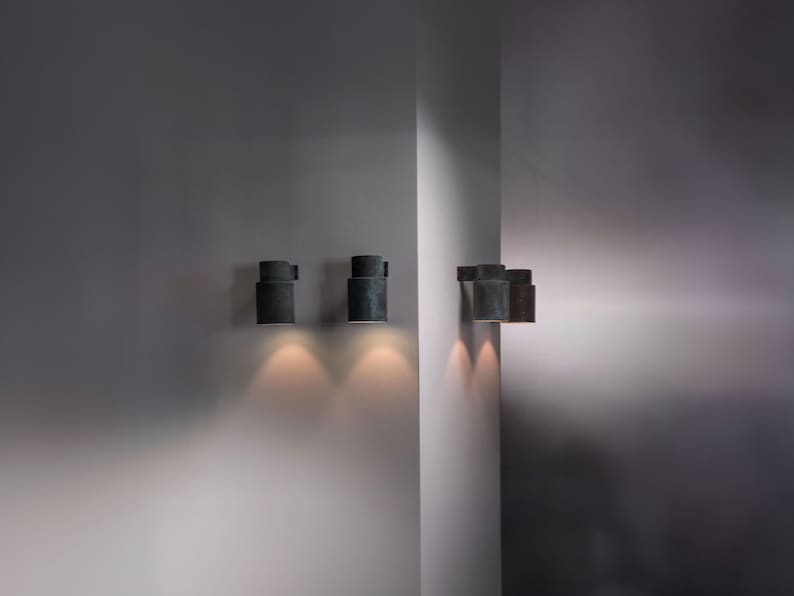 May include: Four black cylindrical wall sconces with a textured finish, mounted on a white wall. The sconces are turned on and casting a warm glow.