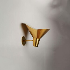 May include: A gold-toned wall sconce with a funnel-shaped shade. The sconce has a circular base and a single arm that extends to the shade.